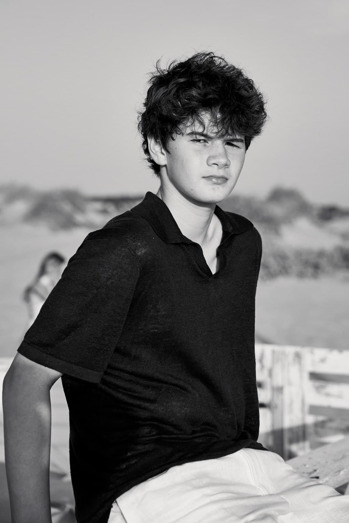 Black-and-white portrait of a teenage boy sitting by the beach
