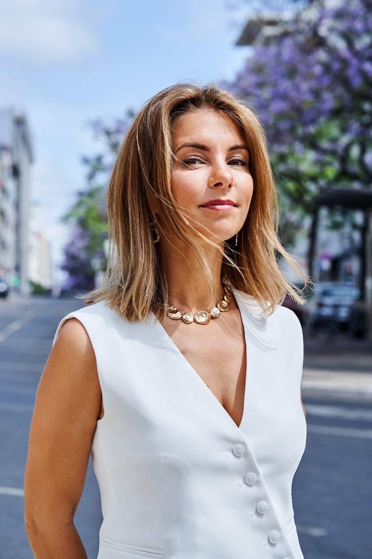 Woman in a white waistcoat on a Lisbon street under a jacaranda tree